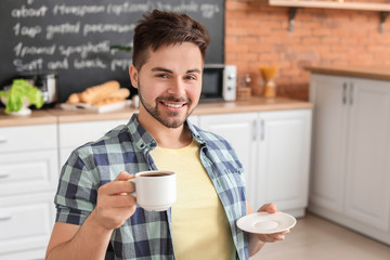 Fototapeta na wymiar Young man drinking hot coffee in kitchen