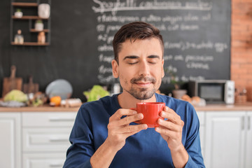 Young man with cup of hot coffee in kitchen