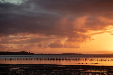 Golden hour sunset with blue and orange clouds, a pier in the water in the foreground and mountains in the background.