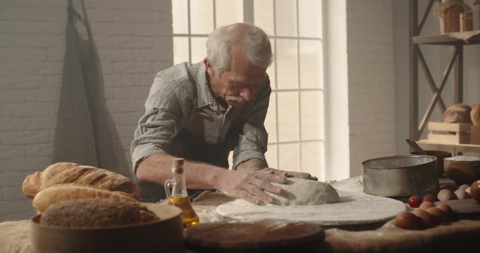 Professional senior moustached caucasian baker forming a bread loaf out of dough with passion, elderly pensioneer enjoying his hobby after retirement 4k footage