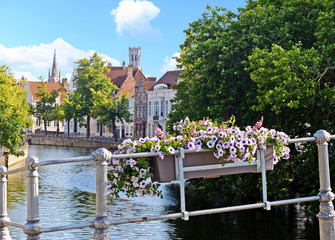 View over Bruges from canal with belfry and church of Our Lady, flower box with violet petunias in...