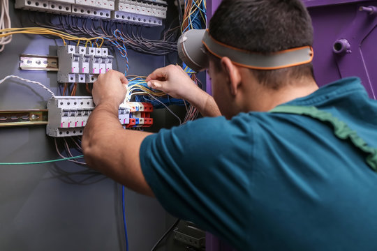 Male electrician with flashlight repairing distribution board