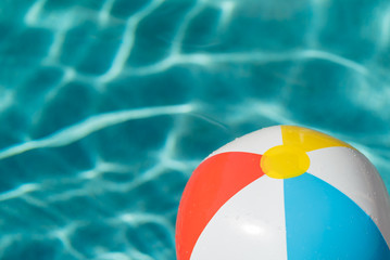 Red, white, yellow and blue beach ball floating on blue water in a pool on a hot summer day