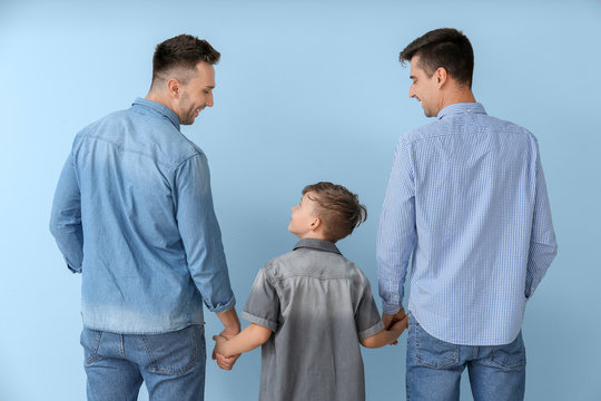 Happy gay couple with adopted child on color background