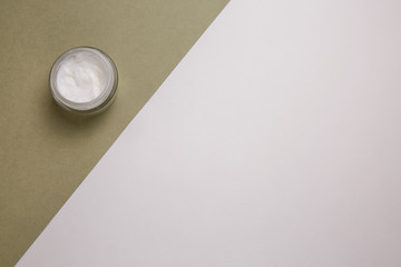 Open jar of cream on the background of white and khaki.