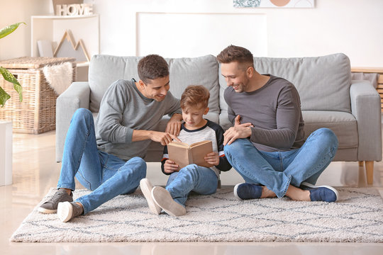 Happy gay couple with adopted child reading book at home