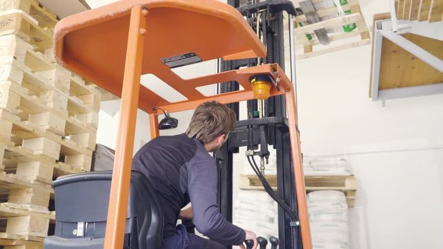 Young caucasian
man industrial worker operating and driving forklift, unloading pallets. 