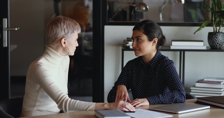 Professional indian saleswoman, insurance broker having business conversation negotiating with client, convincing caucasian business woman customer to buy insurance services. Mentoring, apprentice