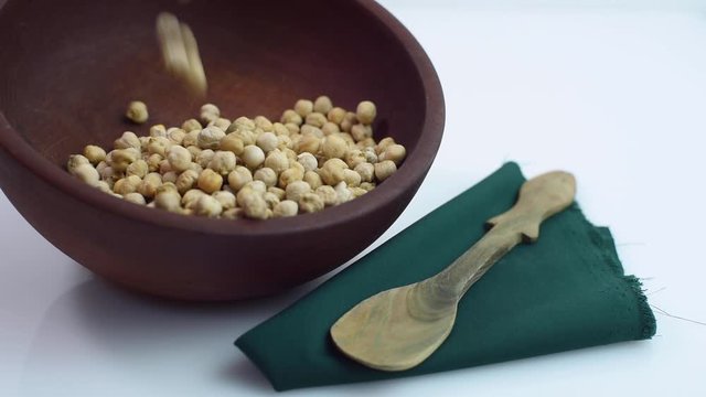
chickpeas falling in wooden bowl with napkin and rustic spoon on white background