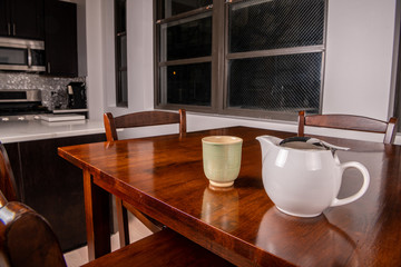 Closeup of a tea cup and tea pot on a wooden table in a modern, city apartment.