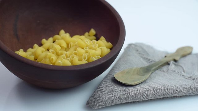 elbow noodles falling in wooden bowl with napkin and rustic spoon on white background