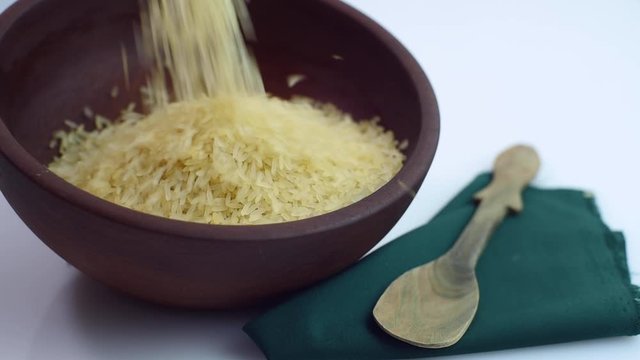 rice falling in wooden bowl with napkin and rustic spoon on white background