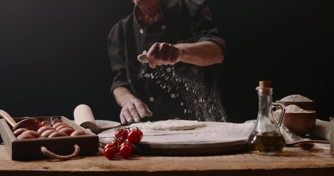 Authentic elderly moustached caucasian chef is making and forming dough for pizza on floured table, using traditional methods and recipe, isolated on black background 4k footage