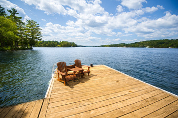 Adirondack chairs sitting on a wood dock facing a lake