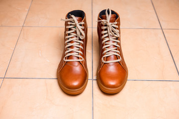 Motorcycling Relative Topics. Closeup of Protective Motorcyclist Leather Tan Sneakers Placed Indoors On Pale Tiles Floor.