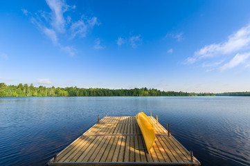 Yellow canoe sitting on a lake wooden dock on a sunny summer morning at the cottage. 