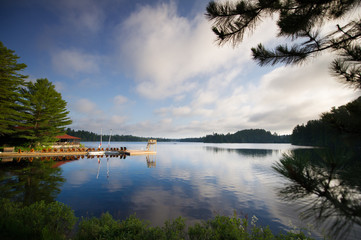 Sunny summer day in Canada. Adirondack and lounge chairs sitting on a wooden dock facing a calm...