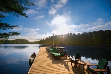 Sunrise over the Algonquin Provincial Park in Canada. Multiple lounge chairs on a wood dock are...