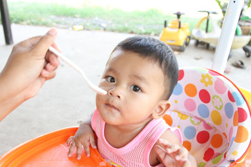 Asian boy 6 months old eating rice porridge and porridge dirty her mouth. Mother feed the son.