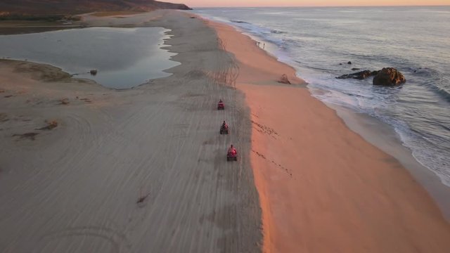 Driving ATV Quad on Sandy Beach by the Ocean. Aerial View of Groip of Vehicles in Cabo San Lucas, Mexico