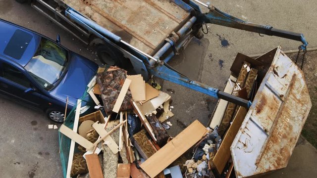 Truck moves fallen garbage container. Trash damaged blue car