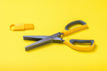 Kitchen scissors with multiple blades and a cleaning tool on a yellow background.