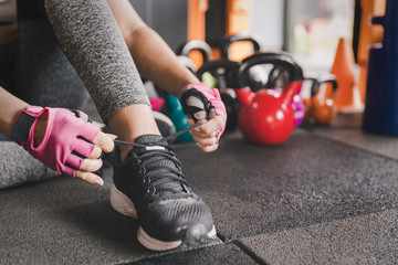 Woman tying shoe with kettlebell weight background prepareing fitness at gym room.Sport relax and healthy life in indoor or sport complex to add strength to the lungs.