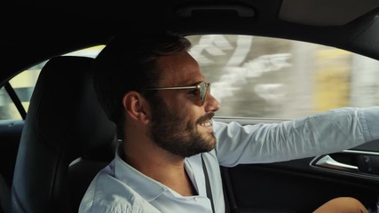 Successful business man driving his luxury car. Happy and fulfilled man in a button-down shirt drives his automobile while he smiles.