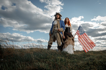 Man in form of officer of War of Independence and girl in historical dress of 18th century. July 4 is US Independence Day. Couple of patriots freedom fighters in outdoor on background cloudy sky - obrazy, fototapety, plakaty
