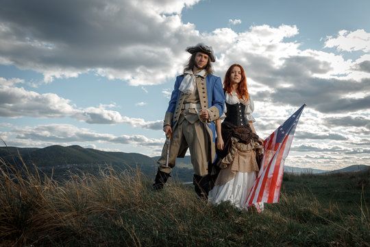 Man in form of officer of War of Independence and girl in historical dress of 18th century. July 4 is US Independence Day. Couple of patriots freedom fighters in outdoor on background cloudy sky