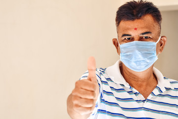 Close up shot of Indian male wearing medical mask and giving thumbs up.