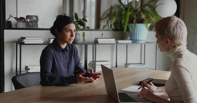 Young indian female applicant talking to company recruiter at job interview. Millennial graduate candidate speaking to employer explaining professional skills at office meeting. Recruiting concept