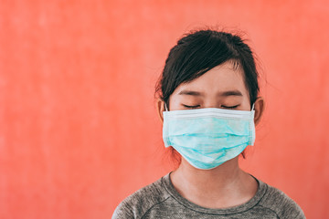 Little asian girl wearing sterile medical mask for protect Covid-19 isolated on red background....