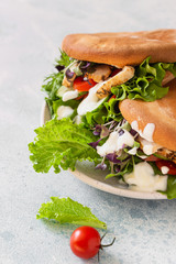 Pita bread sandwiches with grilled chicken, tomato, cucumber, lettuce and sauce served on ceramic plate over grey stone background. Healthy fast food concept. Close up.