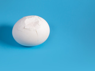 a cracked white large egg on a blue background on the left of the frame