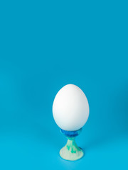 a whole unpainted white egg on a stand on a blue background in the center of the frame