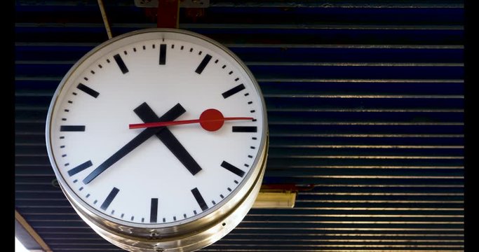 A big clock ticking away in the train station, awaiting on the next train to arrive