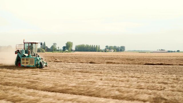 Cinematic aerial drone shots turning around a flax machine going fast through the field