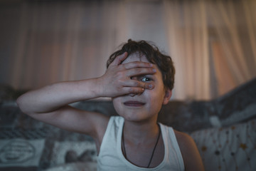 Small emotional boy covers his face with his hand, watching a horror movie