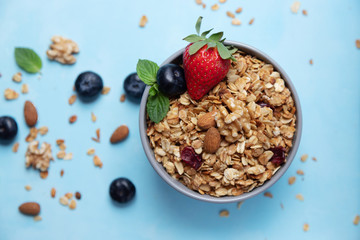 Bowl, cup with homemade granola or oatmeal granola with nuts and fresh strawberries and blueberries. Flakes and berries are scattered nearby.