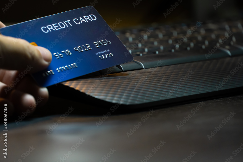 Poster close up Shallow focus hand hold Credit Card on Computer keyboard. Background for E-commerce and online shopping concept.
