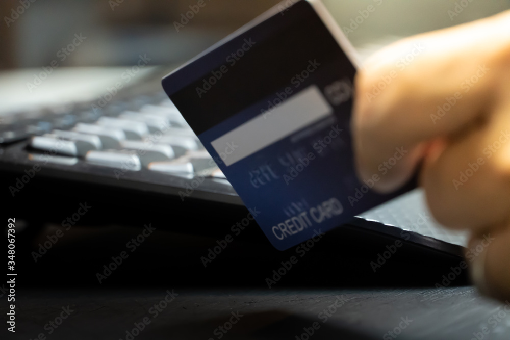 Poster close up Shallow focus hand hold Credit Card on Computer keyboard. Background for E-commerce and online shopping concept.