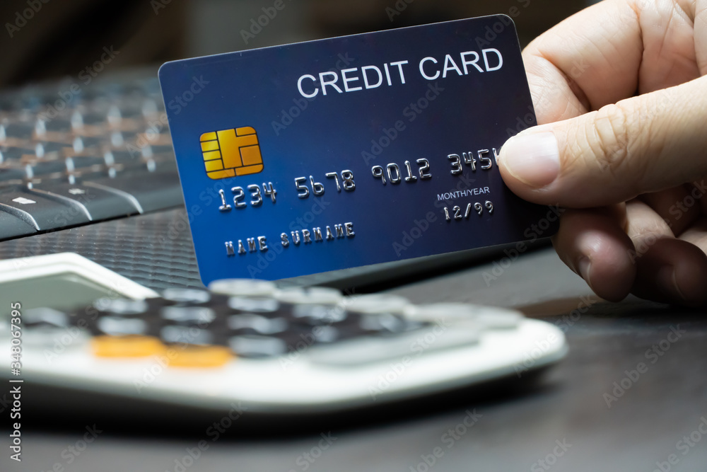 Poster close up Shallow focus hand hold Credit Card with Computer keyboard and calculator. Background for E-commerce and online shopping concept.