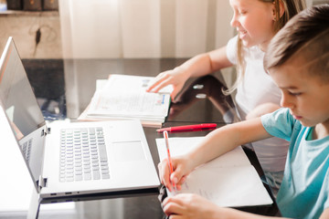 Boy and girl, brother and sister study at home. Children are sitting at a table with open notebooks and a laptop.