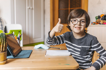 Distance learning for children during the coronavirus epidemic. A boy sits at a table and performs...