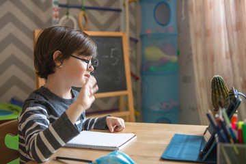 Distance learning for children during the coronavirus epidemic. A boy sits at a table and performs...