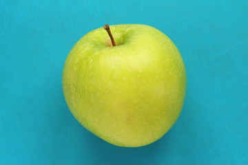 Green yellow apple on a blue background. Juicy ripe beautiful fruit.