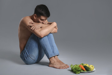 Sick man with fresh vegetables on grey background. Concept of anorexia