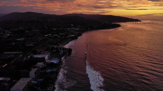 Night falls at the bay of Mancora, dramatic colors reflect on the water, aerial
