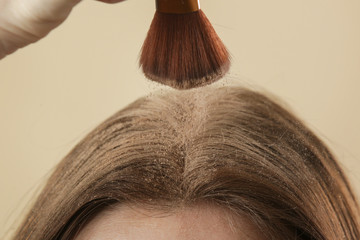 Close up view at woman applaying natural dry shampoo on hair roots. Brunette uses organic non-toxic...